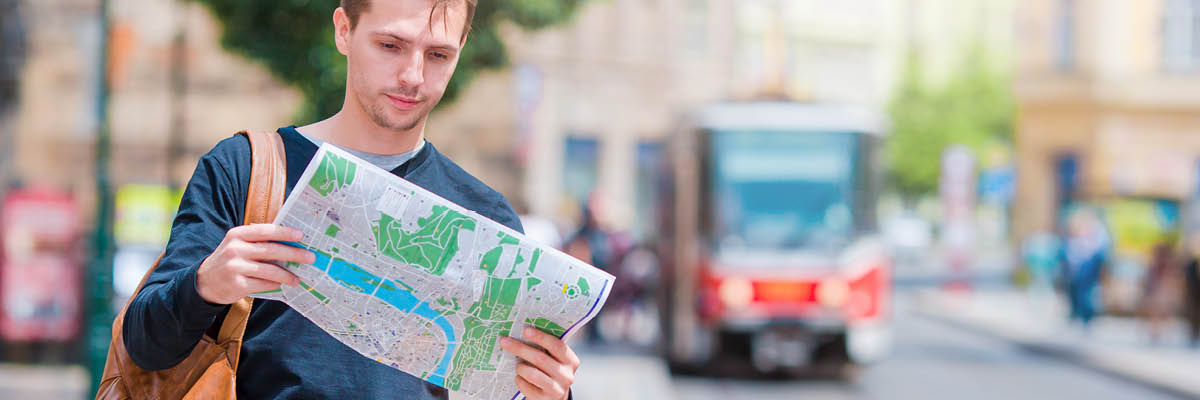 young man with blue pullover looking at a map. In background a bus